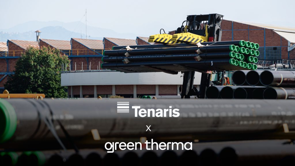 Industrial yard with stacked black pipes and a yellow crane lifting them, green pipe ends visible, backdrop of brick buildings (Tenaris branding partially visible).