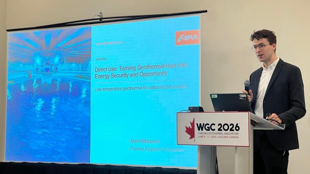 Male presenter at a conference podium giving a talk about geothermal energy (WGC 2026) with a large blue screen slide behind him.