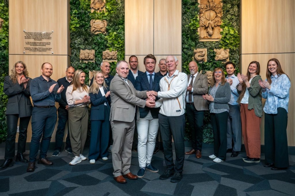 Gas management photo 1 | ThinkGeoEnergy - Geothermal News & Insights Group of professionals stands together in a lobby, two men in center shake hands as others applaud behind them.