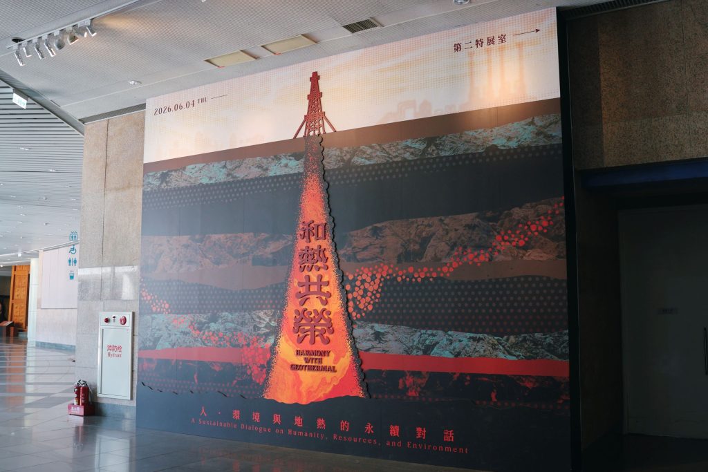 Exhibit front | ThinkGeoEnergy - Geothermal News & Insights Indoor wall mural featuring a volcanic eruption graphic with red Chinese characters and the subtitle 'Harmony with Geothermal' alongside the date 2026.06.04 in an exhibition hall.