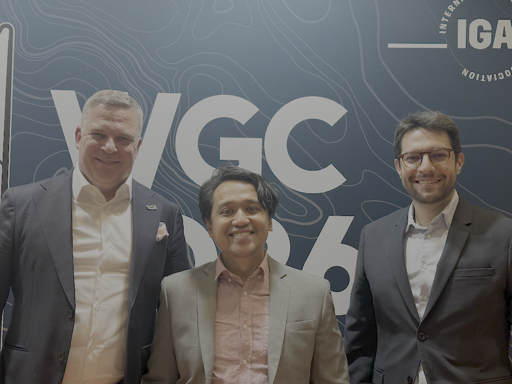 TGE_team_wgc2026 | ThinkGeoEnergy - Geothermal News & Insights Three men in suits pose and smile for a photo in front of a blue backdrop featuring the VGC logo.